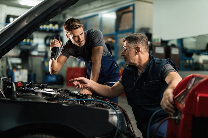 auto-mechanics-communicating-while-doing-diagnostic-of-air-conditioning-system-in-a-workshop.jpg